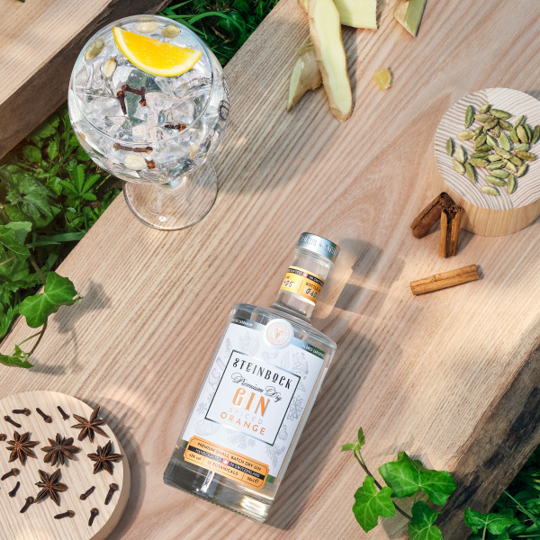 Steinbock Spiced Orange Gin & Tonic Cocktail auf einem Holzbrett mit Botanicals